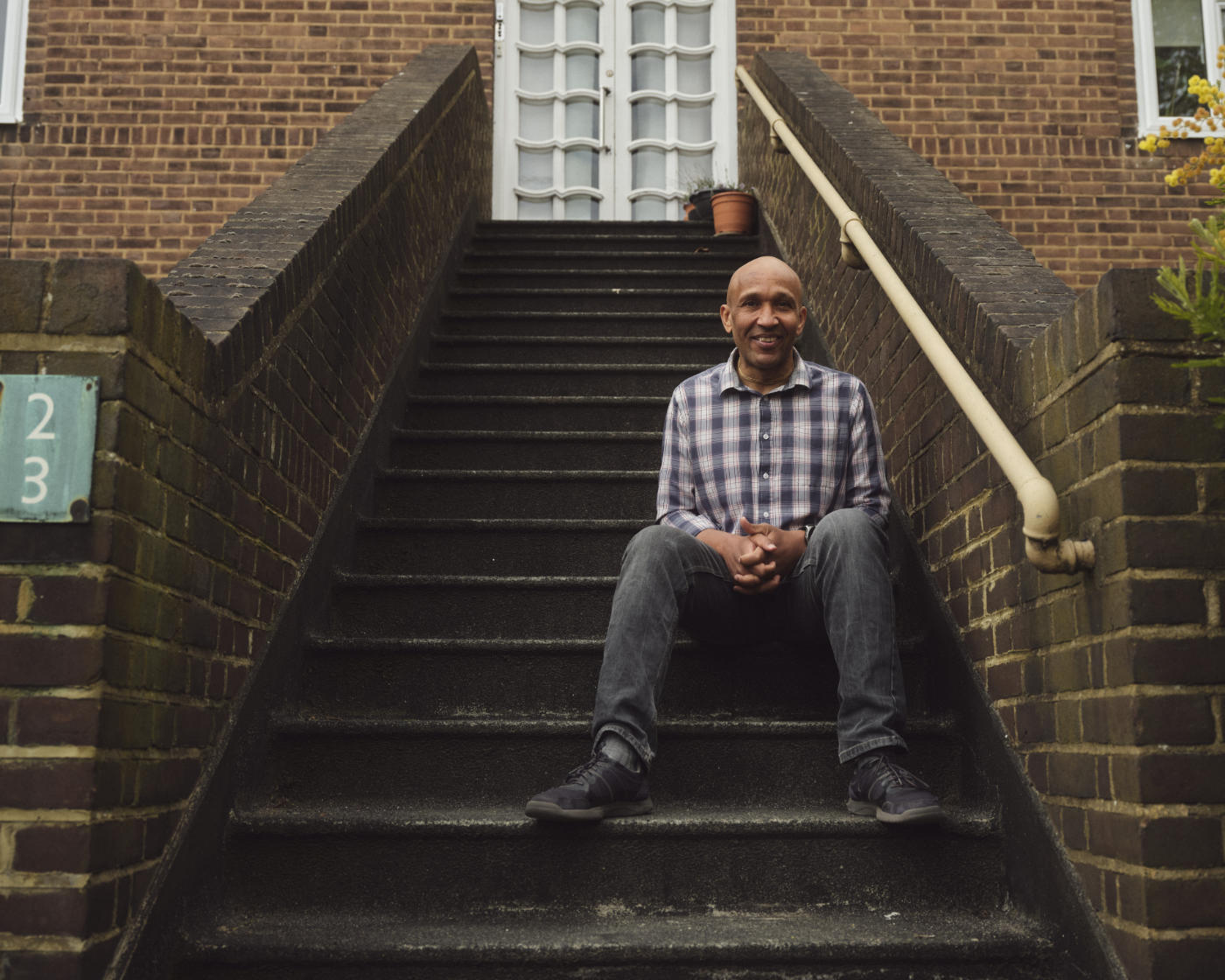 A man sits on the outdoor steps of his housing complex, smiling at the camera