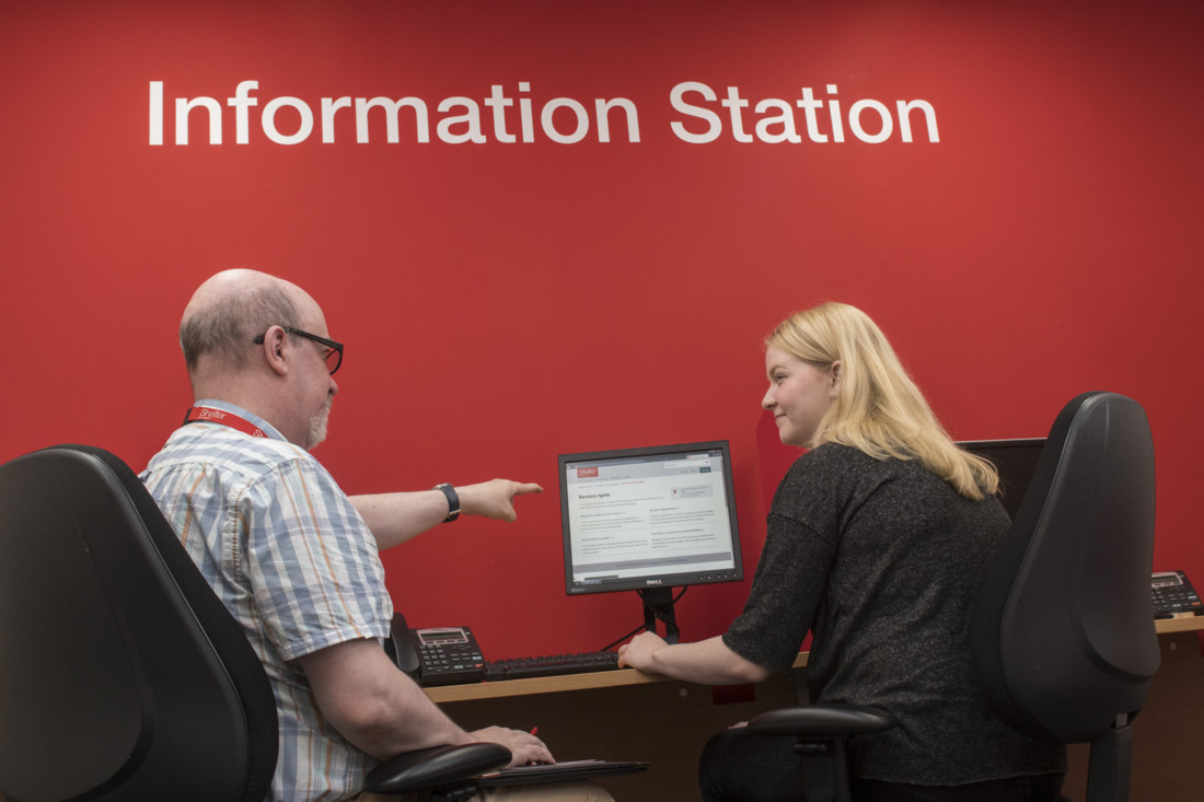 Man and woman at an 'Information Station' in a Shelter hub, looking at housing information on a website.