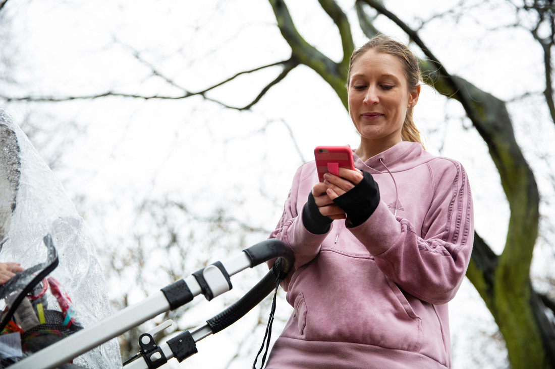 Woman looking at her mobile phone, with a child in a stroller.