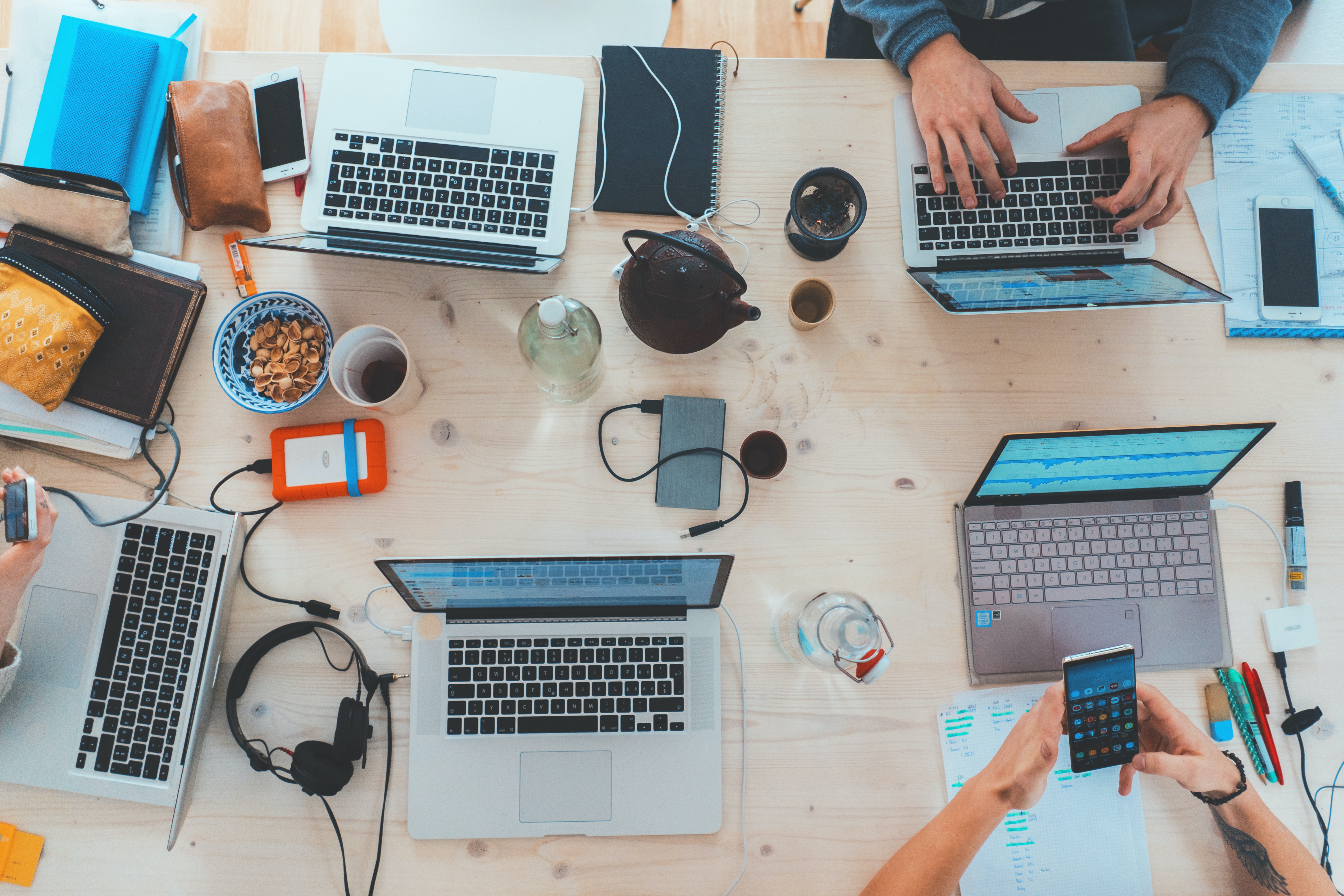 Overhead photo of a table covered with laptops, mobile phones and tablets, with hands of people using them.