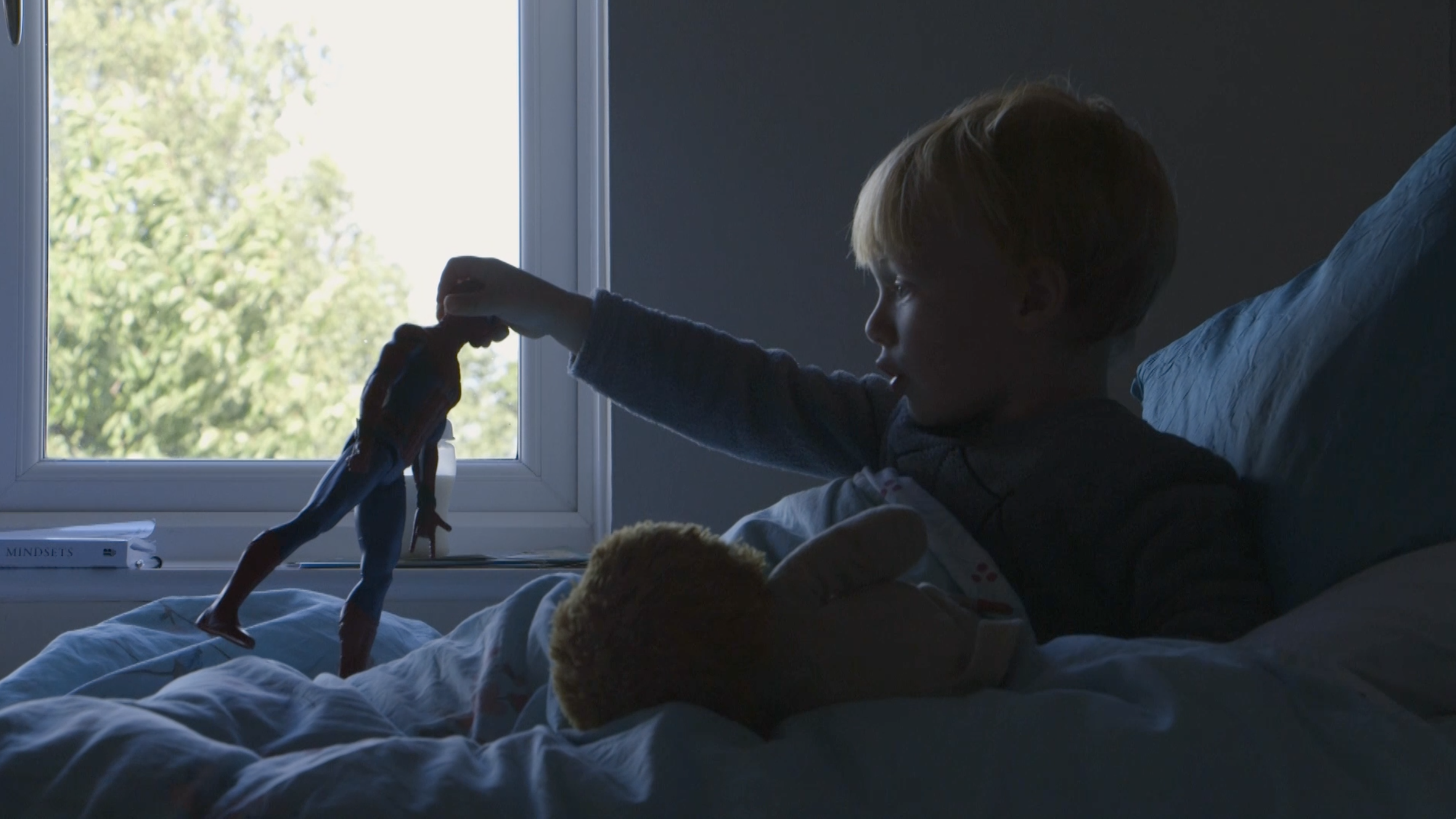 Screen capture of a Shelter video, showing a young boy in bed with a toy.