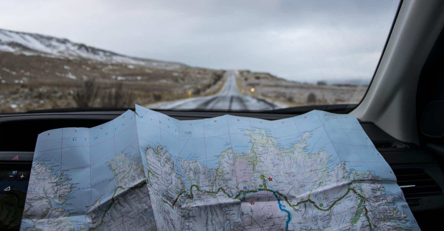 Image of a roadmap inside a car, with a road ahead outside the window.