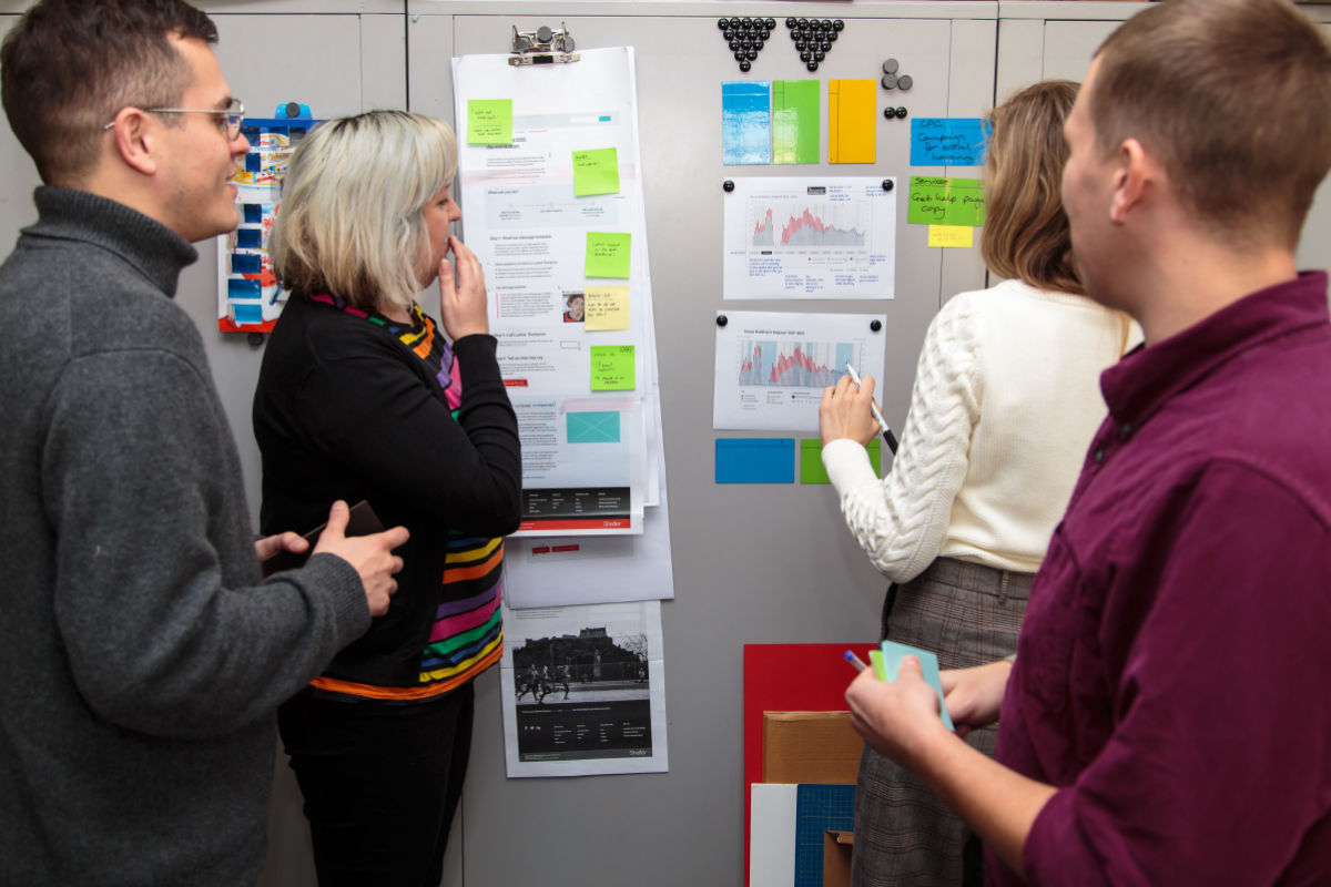 4 digital workers at Shelter consider diagrams pinned to a board